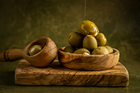 A still life painting of olives in a wooden bowl with a wooden spoon